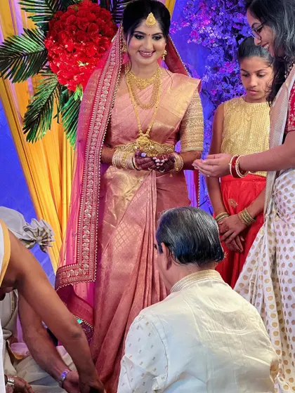A candid moment from a wedding ceremony. The bride's pink brocade saree is draped perfectly, allowing her to participate in the rituals with ease.