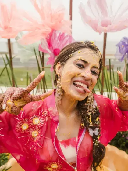 The bride shows off her playful side, sticking her tongue out for a fun photo amidst the haldi chaos. Her vibrant personality shines in this candid moment.