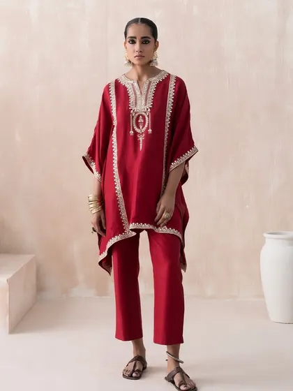 A clean, full-length lookbook shot for Saisha's "Firdaus" collection. The red embroidered kaftan is styled with simple, traditional footwear to keep the focus entirely on the garment's design and fit.