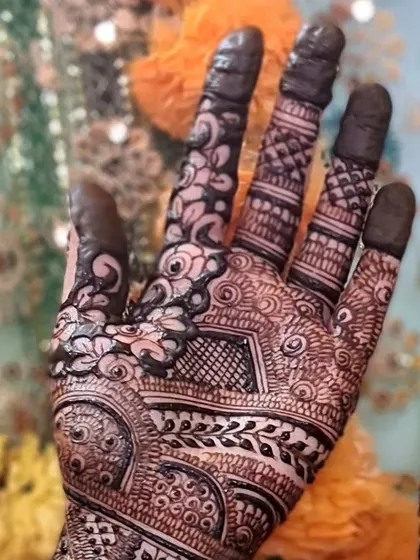 A close-up of the intricate work on a bride's palm and fingers, showing a mix of floral, leaf, and checkerboard patterns.