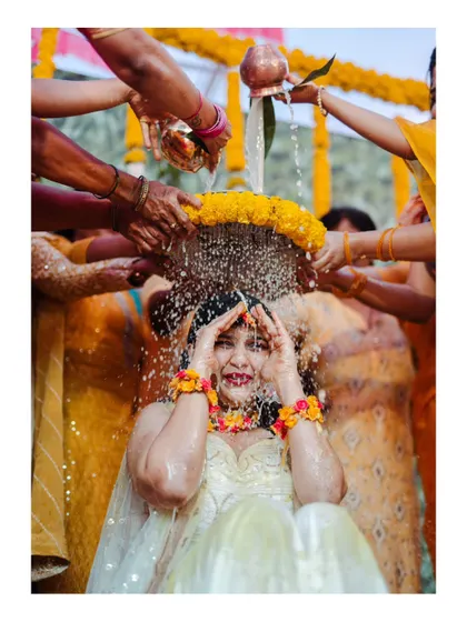 A joyful moment as the bride is showered with holy water and flowers during her Haldi ceremony.