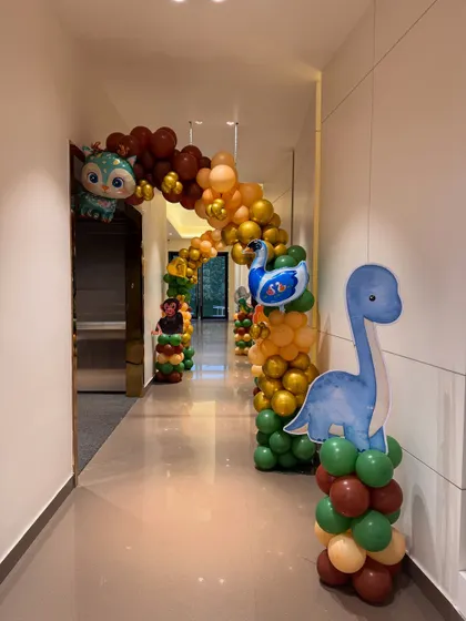 A whimsical balloon archway with dinosaur and animal characters creates a fun and inviting entrance corridor for a kids' party.