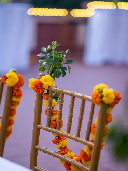 A close-up shot of a chair decorated with vibrant orange and yellow marigold garlands, showcasing the small but impactful details that bring a traditional event to life.