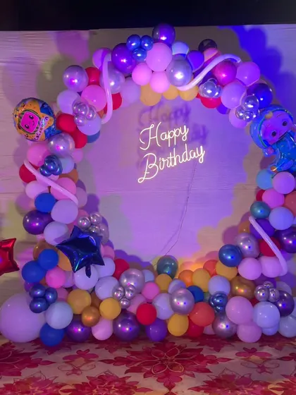 A vibrant and colorful Cocomelon theme with a multi-colored balloon ring, character foil balloons, and a neon 'Happy Birthday' sign.
