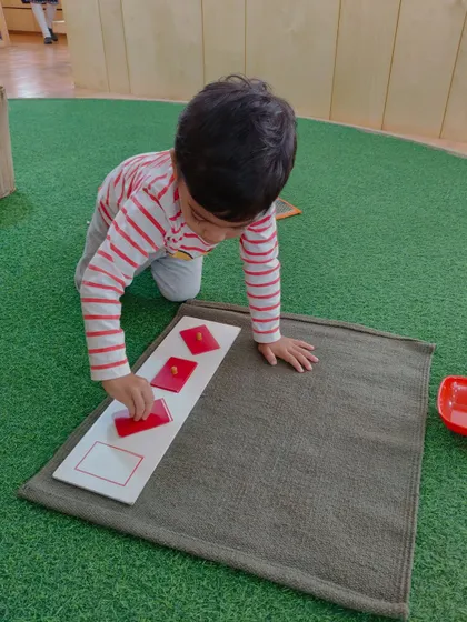 A child works with a set of red geometric cards on a mat. Using a designated work mat helps the child define their personal space and brings a sense of order and focus to their chosen activity.