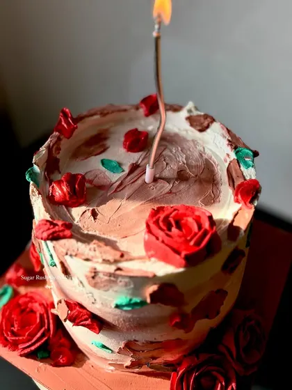Another view of this beautiful rustic cake, with a single lit candle. The combination of chocolate and vanilla frosting with red rose details is simply stunning.