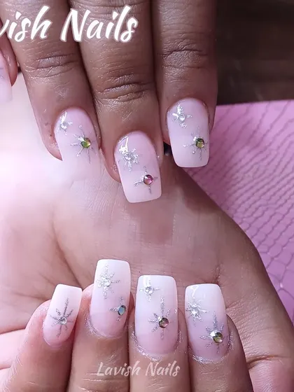 A delicate and dreamy set of milky white nails adorned with scattered starburst crystals in various colors for a whimsical sparkle.