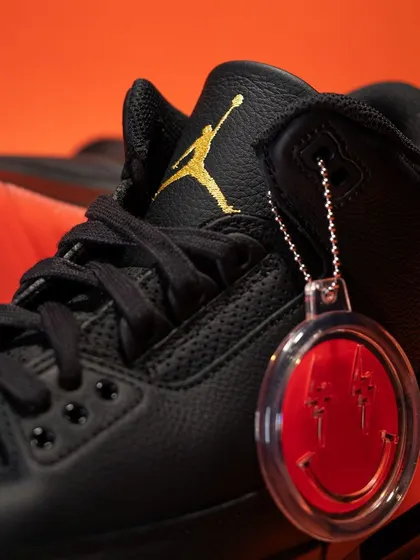 Close-up on the J Balvin 'Rio' Jordan 3, focusing on the iconic smiley face hangtag and the gold Jumpman logo on the tongue.