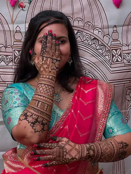A classic bridal pose, covering one eye with a henna-adorned hand. This highlights the dense patterns on the palm and forearm.