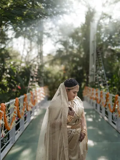 A bride on a bridge, bathed in ethereal sunlight filtering through the trees. The veil and the light create a dreamy, angelic atmosphere.
