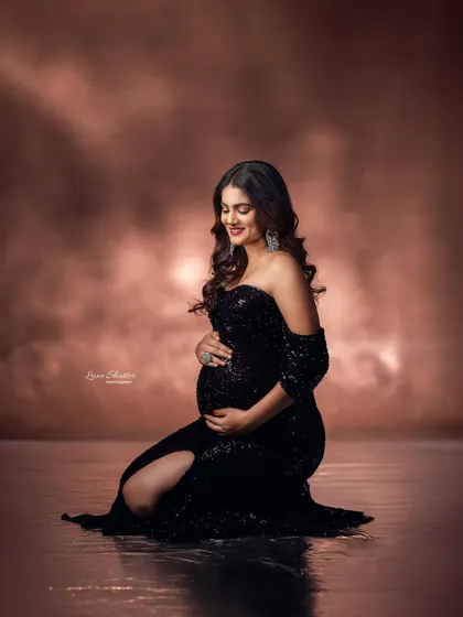 This kneeling pose is both elegant and powerful. The light catches the sequins on the black gown, adding a touch of sparkle to this glamorous maternity portrait.