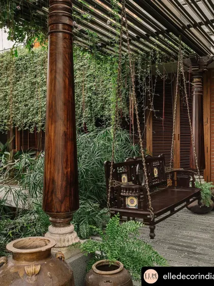 An outdoor space should be lived in and enjoyed. This traditional wooden swing, nestled among ferns and hanging vines in a Valsad home, creates a perfect, cozy corner for relaxation, seamlessly blending heritage furniture with a lush, tropical garden setting.