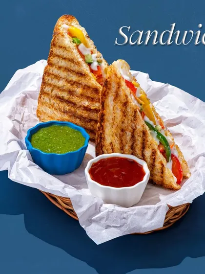 A grilled vegetable sandwich, cut diagonally and served with ketchup and mint chutney.