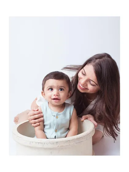 A mother playing with her baby, who is sitting in a rustic pot prop.