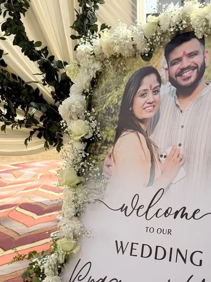 A personalized welcome sign for Pragya & Yash's wedding, framed with white flowers and set at the beginning of the beautifully decorated entrance path.