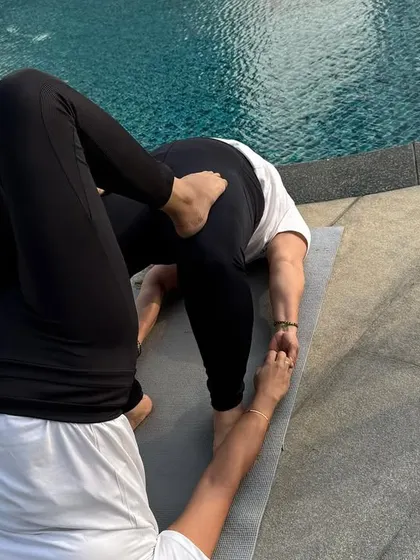 A partner inversion by the pool, combining a shoulder stand with a supportive base. This advanced work is built on a foundation of trust and clear communication.