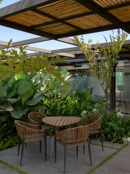 A quiet seating nook at Brigade Oasis, surrounded by lush greenery. The pergola with a bamboo canopy provides shade, making it a perfect spot to relax and enjoy the connection between the architecture and the landscape.