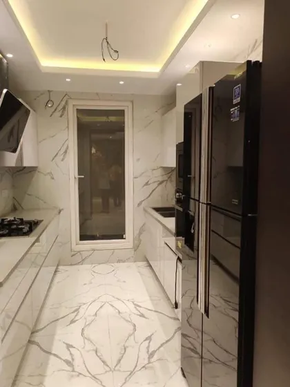 A stunning parallel kitchen that uses large-format marble-look tiles on the floor and walls for a seamless, luxurious feel. The white handleless cabinets and integrated appliances enhance the minimalist aesthetic.