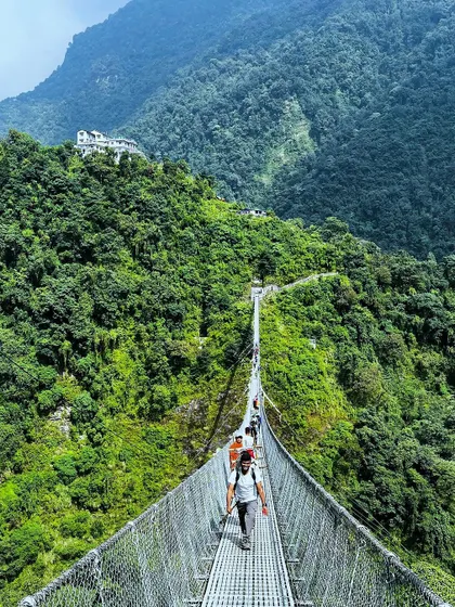 Trekkers make their way across a long suspension bridge high above a river in the Annapurna region, a thrilling and essential part of the Himalayan experience.