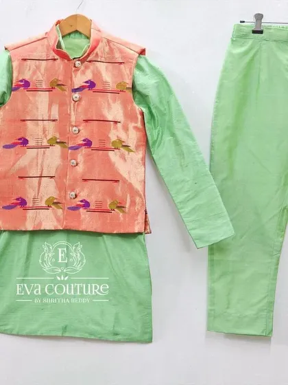 A three-piece boys' set with a Paithani jacket. The light green kurta and pajama are paired with a peach-colored jacket that has woven Paithani motifs.