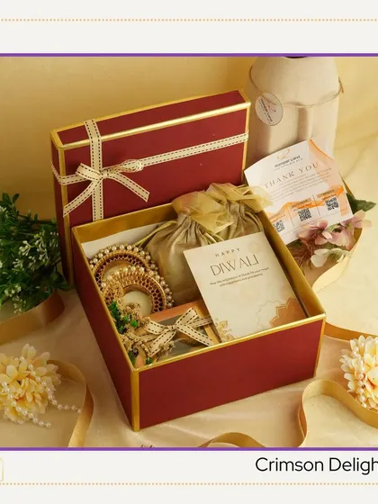 This "Crimson Delight" hamper is presented in a rich red and gold box. It includes a decorative diya and a potli bag, adding a traditional touch to the festive goodies inside.