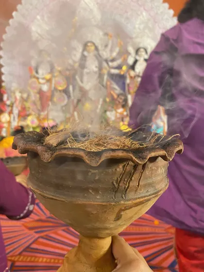 A close-up of the dhunuchi, the earthen pot filled with burning coconut husk and incense. The smoke is central to this ritual dance, creating a mystical and fragrant atmosphere.