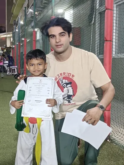 A young boy proudly displays his new belt and certificate. He is on the path to becoming a black belt.