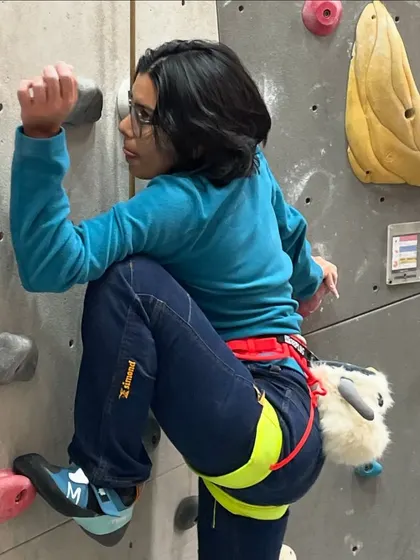 A first time climber focuses on her footwork and grip as she makes her way up a beginner route. Notice her chalk bag, an essential piece of gear we provide to help with grip.
