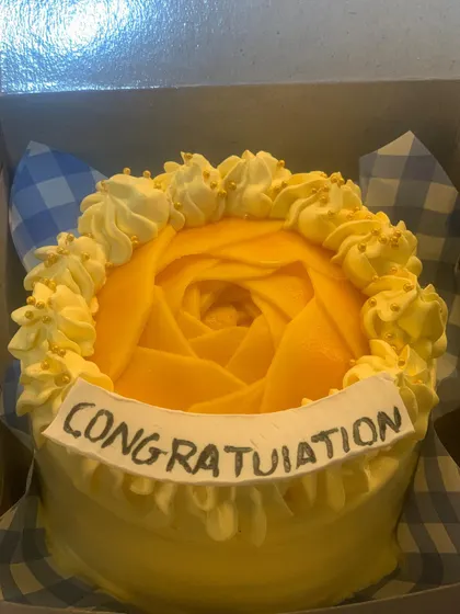 A bright yellow cake with a mango jelly topping carved into a rose. The piped border and "Congratulations" message make it perfect for celebrating an achievement.
