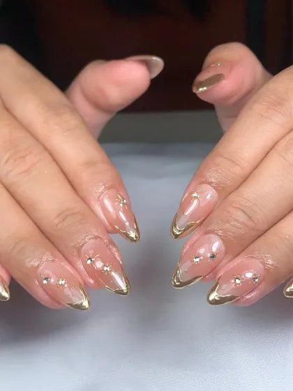 Simple elegance with a touch of sparkle. This design features a sheer nude base, delicate gold-painted tips, and a constellation of tiny rhinestones.