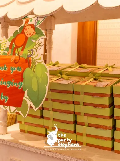 A closer look at the party favor station, showing the neatly stacked gift boxes and the charming 'Thank you for swinging on by' sign with a monkey illustration.