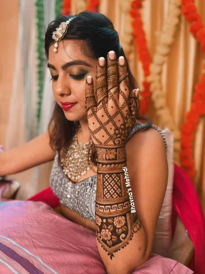 A bride looking elegant while showcasing her detailed back hand mehndi. The design features a beautiful floral band and a classic grid pattern, perfect for a sophisticated bridal look.