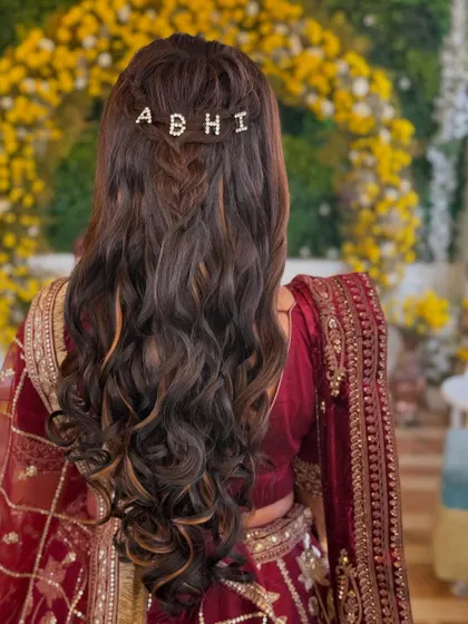 A personalized touch for the Mehendi hairstyle. The custom hair clip with the groom's name adds a sweet and unique detail to her beautiful soft curls.
