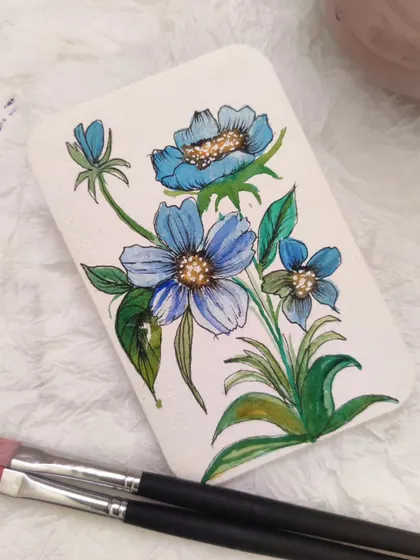 A delicate painting of small blue flowers with gold accents. Adding a touch of metallic paint can bring a magical quality to your watercolor art.