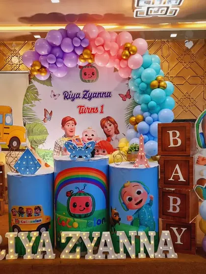 A full view of Riya Zyanna's Cocomelon party, showing the complete arrangement with the iconic bus, character cutouts, and a beautiful pastel balloon arch.