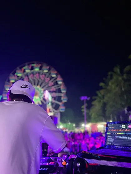 A beautiful shot from behind the decks at a night festival, with the colorful lights of a Ferris wheel creating a magical backdrop.