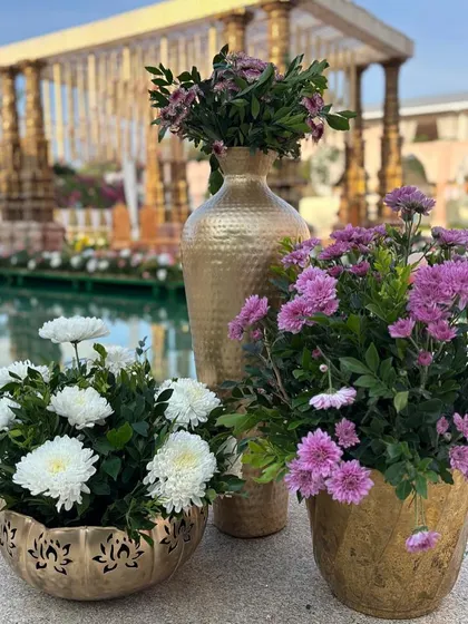 A beautiful arrangement of white and purple flowers in golden pots, set against the backdrop of a floating mandap.