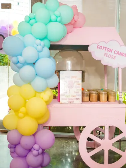 A pink cotton candy cart with a pastel balloon arch, ready to spin sweet treats for guests.