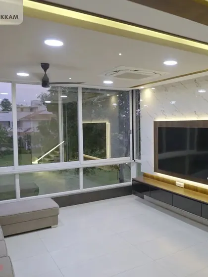 A grand, sunlit living room in the Ayyapakkam villa, with a large TV unit, comfortable L-shaped sofa, and floor-to-ceiling windows.