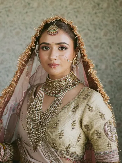 A bridal portrait that exudes quiet confidence and grace. The focus here is on the intricate jewelry and the soft, regal tones of her pastel lehenga.