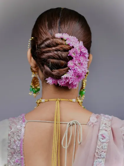 This is the kind of high-end, polished work you'll learn to create. This detailed shot shows a twisted bridal bun, perfectly adorned with a crescent of fresh pink flowers, a style that is both elegant and timeless.