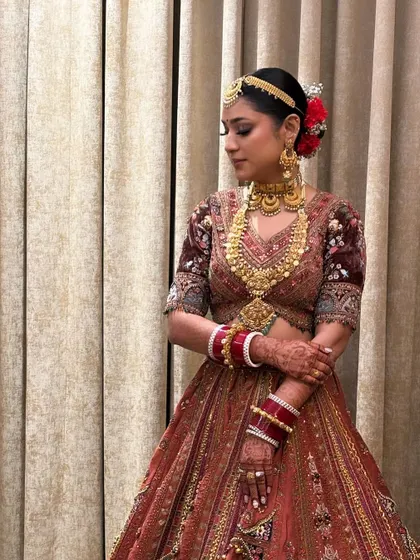 A full view of the traditional bridal look, with a sleek center-parted bun adorned with vibrant red flowers and a matha patti. This is a quintessential bridal hairstyle you will learn to create.