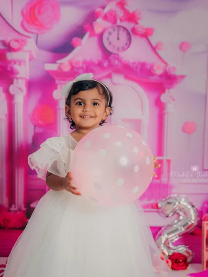 This little 2-year-old is all smiles during her Barbie-themed birthday session, complete with pink balloons and a dreamhouse backdrop.