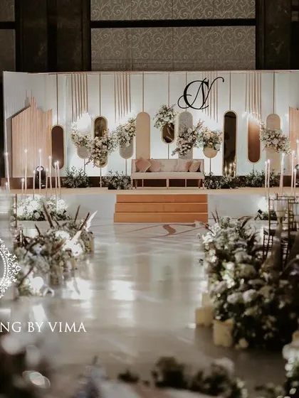 A classic and elegant reception setup symbolizing everlasting love. The stage features a modern, minimalist backdrop with custom monograms, floral arrangements, and soft lighting.