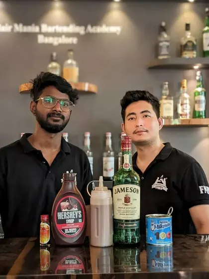 Two students pose with the ingredients for a chocolate and whiskey-based cocktail.