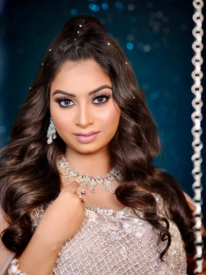 A direct and powerful portrait showcasing a finished sangeet look. The makeup emphasizes the eyes with a dark liner and full lashes, balanced by a neutral lip and perfectly sculpted features.