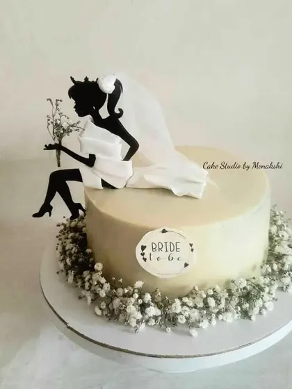 A beautiful bachelorette cake featuring a bride-to-be silhouette topper. The cake is surrounded by a wreath of fresh baby's breath for a delicate and elegant touch.
