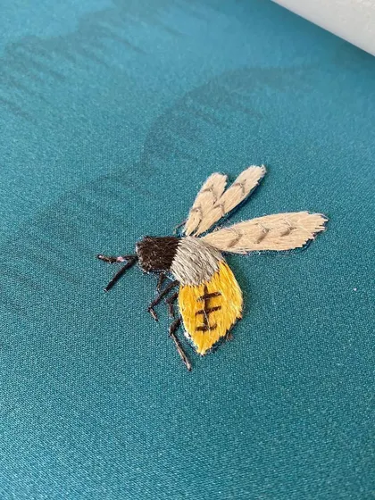 A beautifully detailed embroidered bee from the 'Folly' wallpaper. This tiny detail showcases the artistry and precision that goes into creating these luxurious, hand-finished wallcoverings.