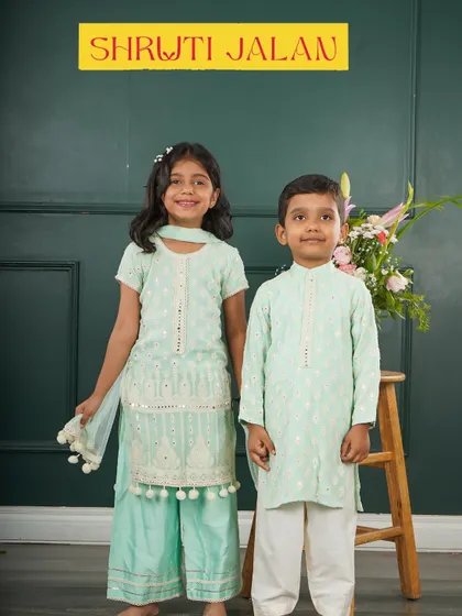 This brother and sister are wearing one of my favorite combinations: a mint green mirror-work kurta for him and a matching sharara set with pom-pom details for her. It’s a fresh and elegant look for any occasion.