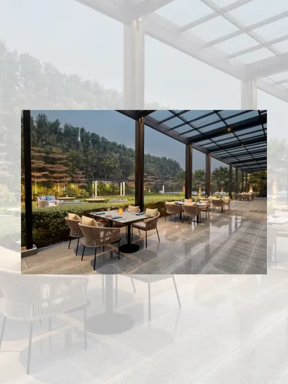 The outdoor dining terrace at the Courtyard by Marriott. The space is covered by a modern pergola with a glass roof, allowing for alfresco dining with views of the hotel's green lawns.
